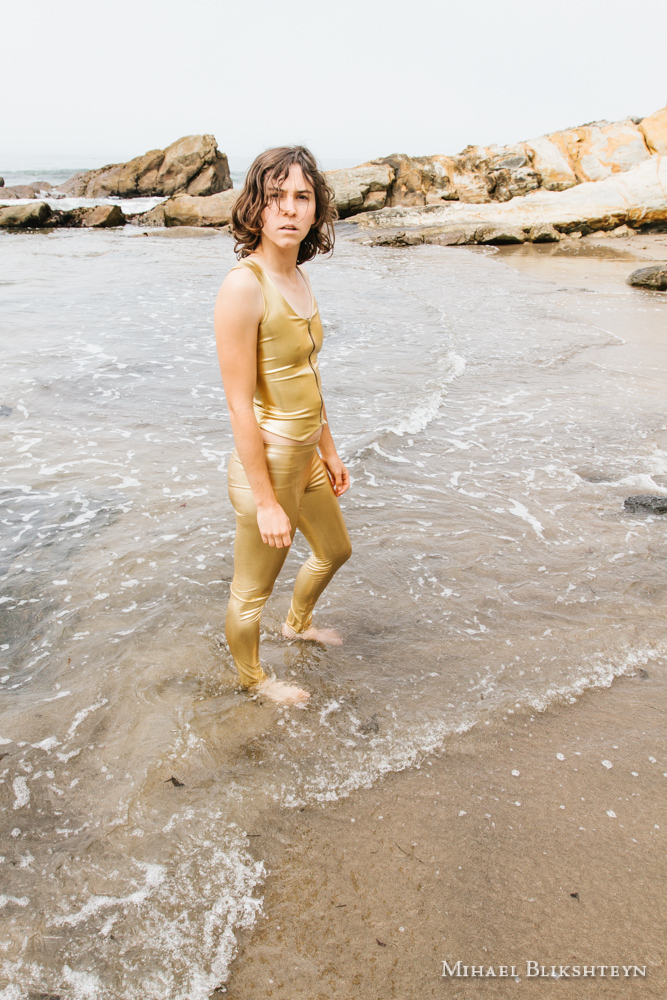 Young woman in golden space suit on matching yellow rocks on a beach