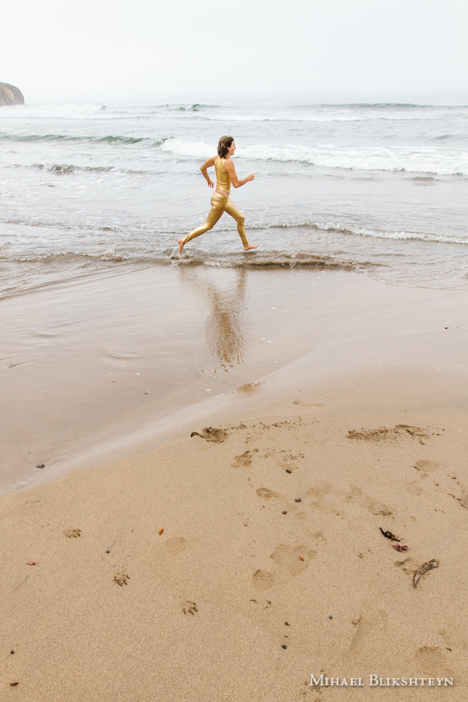 Young woman in golden space suit on matching yellow rocks on a beach