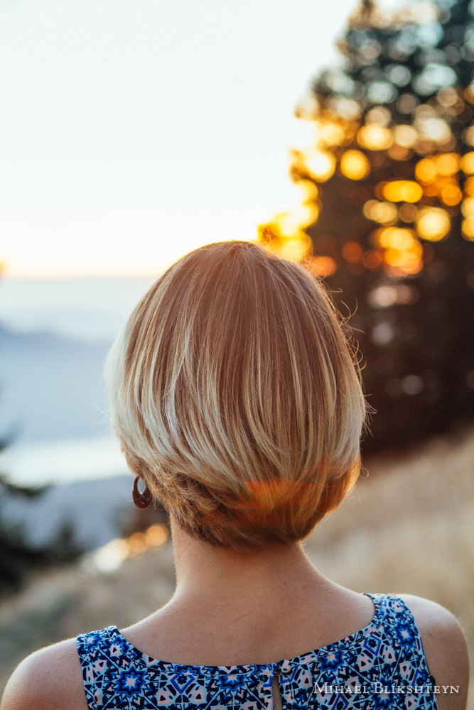 Back of a young woman's head and shoulders as she is watching sunset