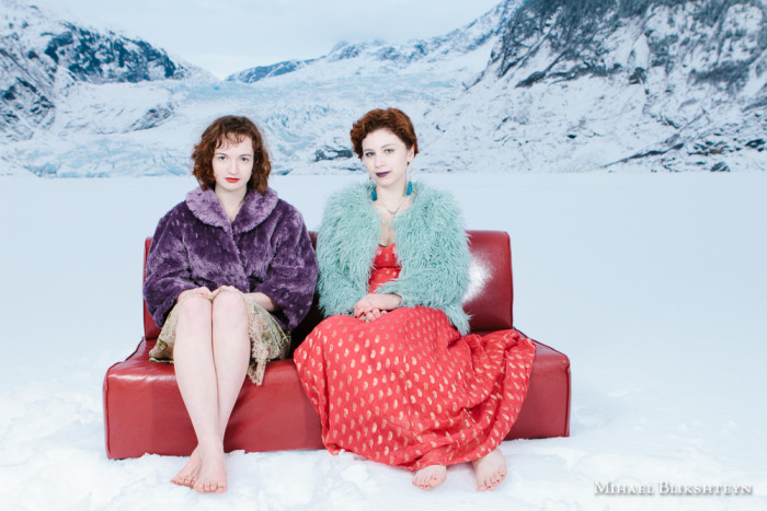 Two young women posing on a red couch in the middle of a frozen lake in front of a glacier in the winter
