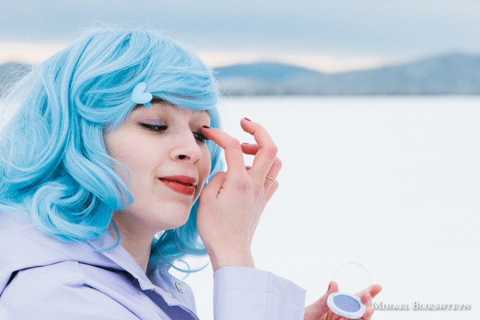 Young woman in blue wig and purple plastic coat applying purple