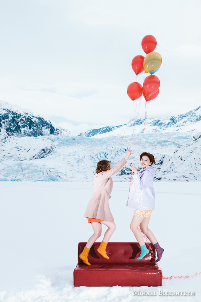 Two young women flying off a red couch on helium balloons in fro