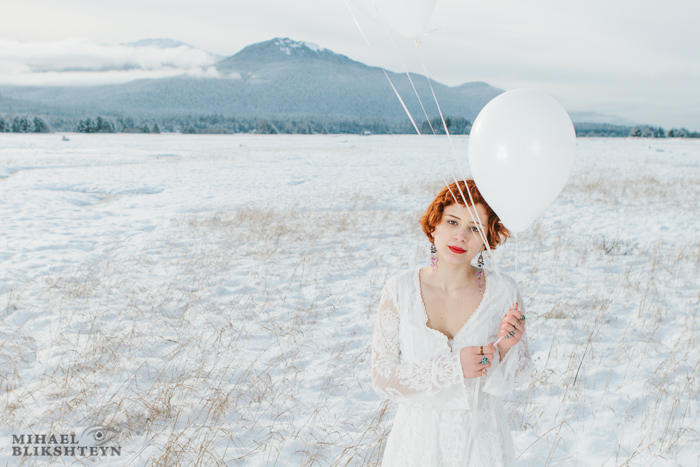 Young woman in white dress holding white balloons on a white snow-covered meadow