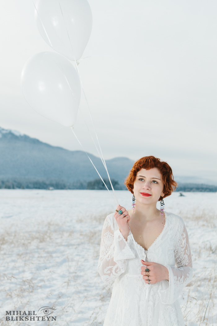 Young woman in white dress holding white balloons on a white snow-covered meadow