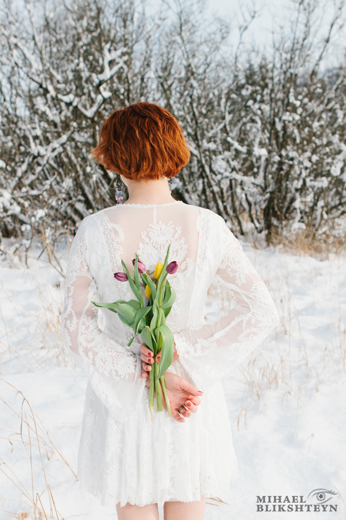 Young woman in white dress hiding bouquet of tulip flowers behin