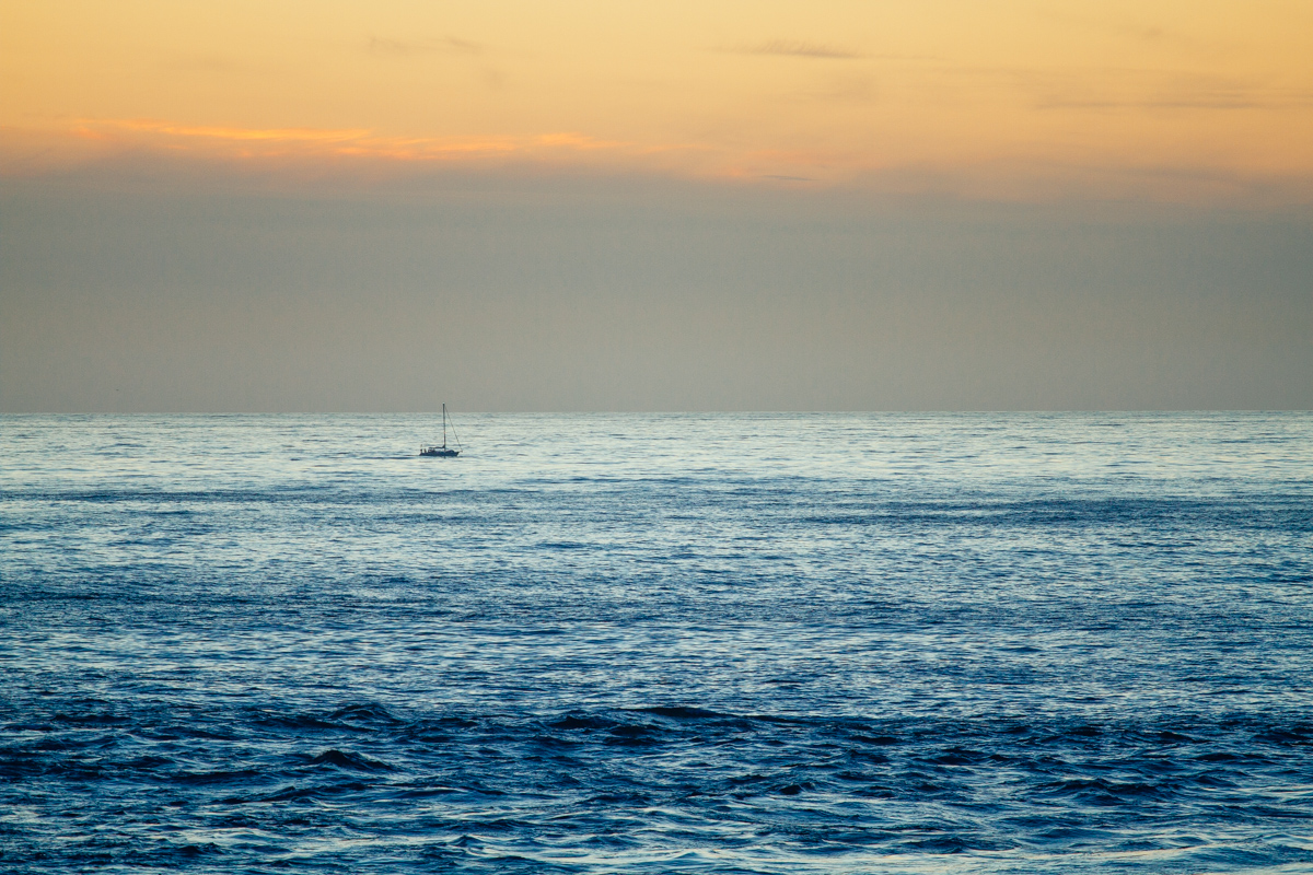 Lone sailboat in the calm, open ocean at sunset